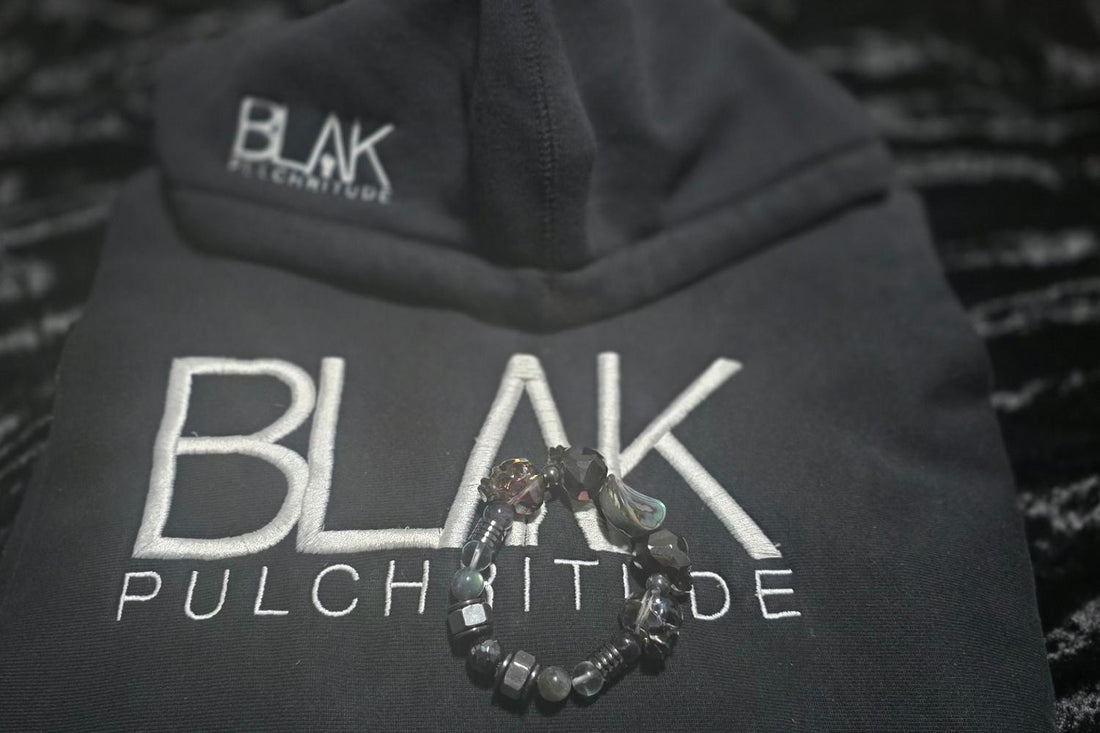 Black BLVK Pulchritude hoodie with two luxury JvOR crystal bracelets placed on top, showcasing the collaboration of intentional jewelry and streetwear