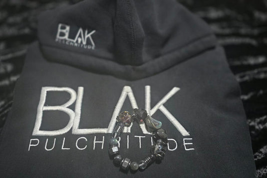 Black BLVK Pulchritude hoodie with two luxury JvOR crystal bracelets placed on top, showcasing the collaboration of intentional jewelry and streetwear